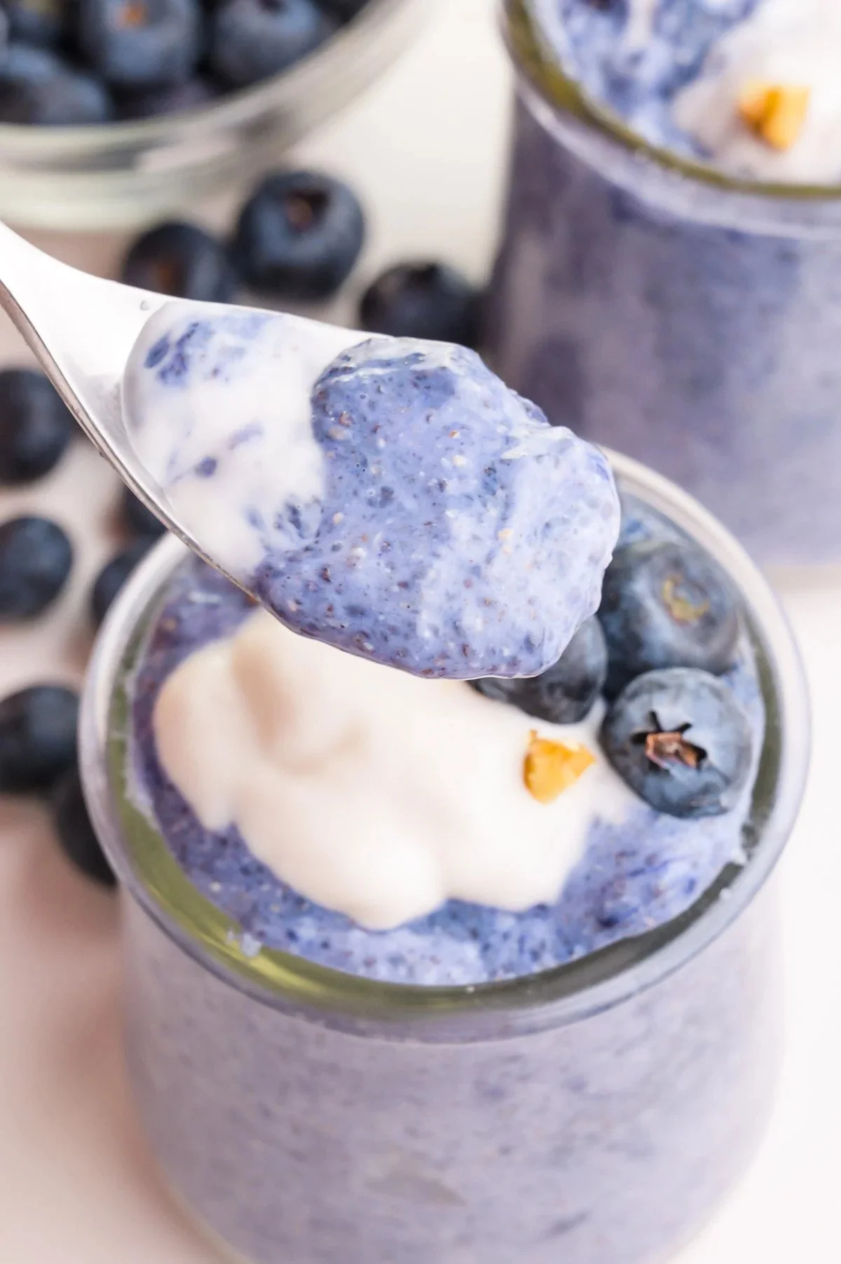 Close-up of a spoonful of blueberry chia seed pudding with coconut yogurt, served in a glass jar with blueberries and a small piece of walnut on top.