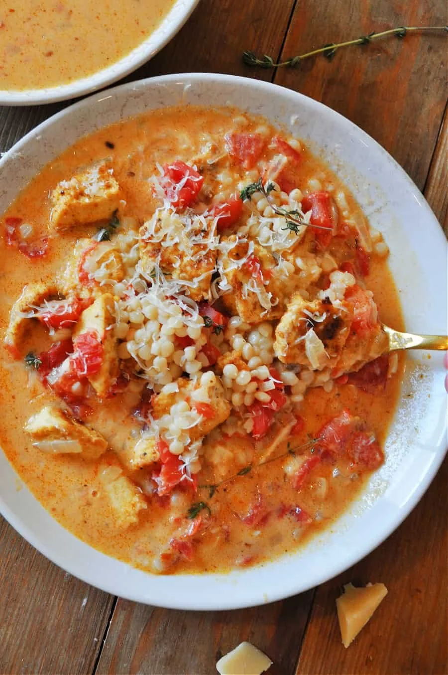 A bowl of vegan soup with diced tomatoes, cheese, and herbs on a wooden table.