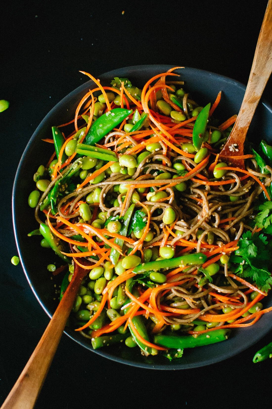 A bowl of Asian-style vegetable noodle salad with shredded carrots, edamame, snow peas, and cilantro.