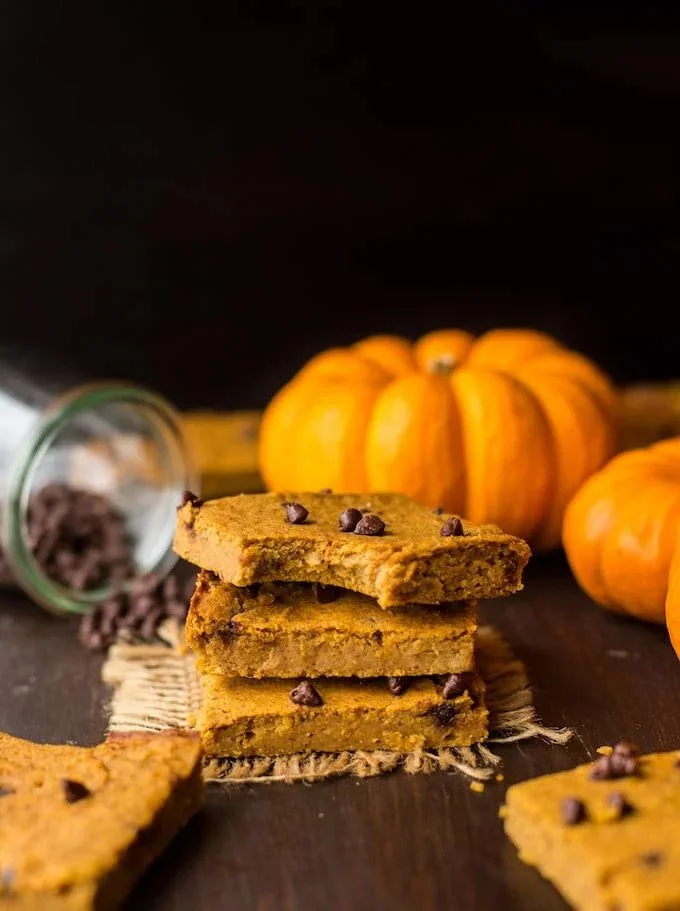 Stacked vegan chocolate chip pumpkin cookies with pumpkins in the background on a dark surface.
