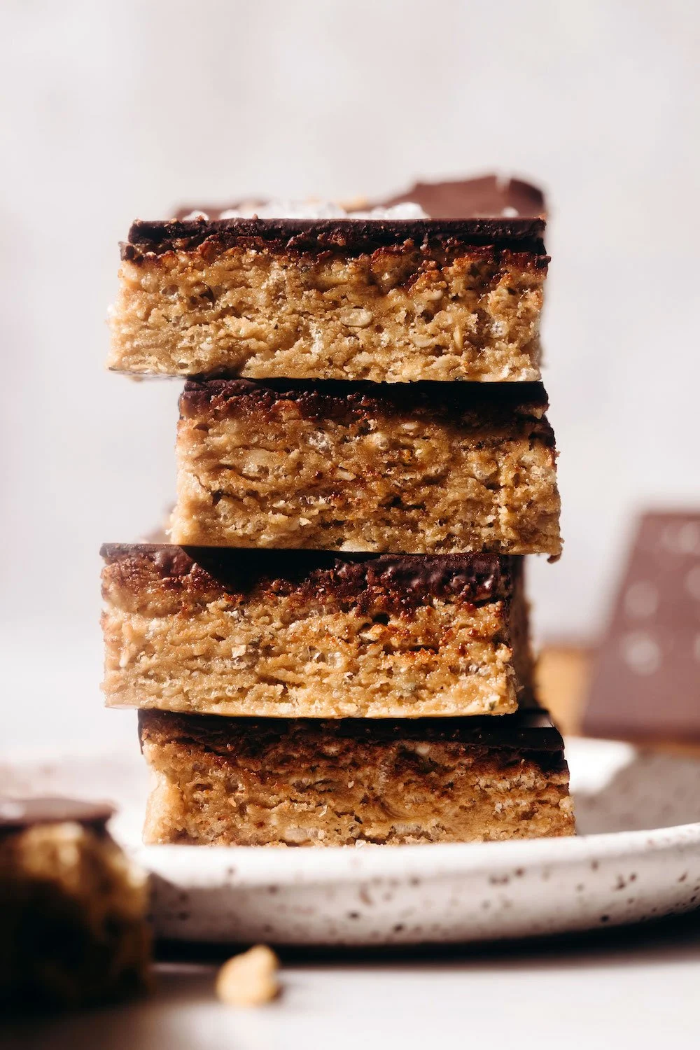 A stack of four caramel peanut rice crispy treats with a chocolate topping on each piece, on a white plate.