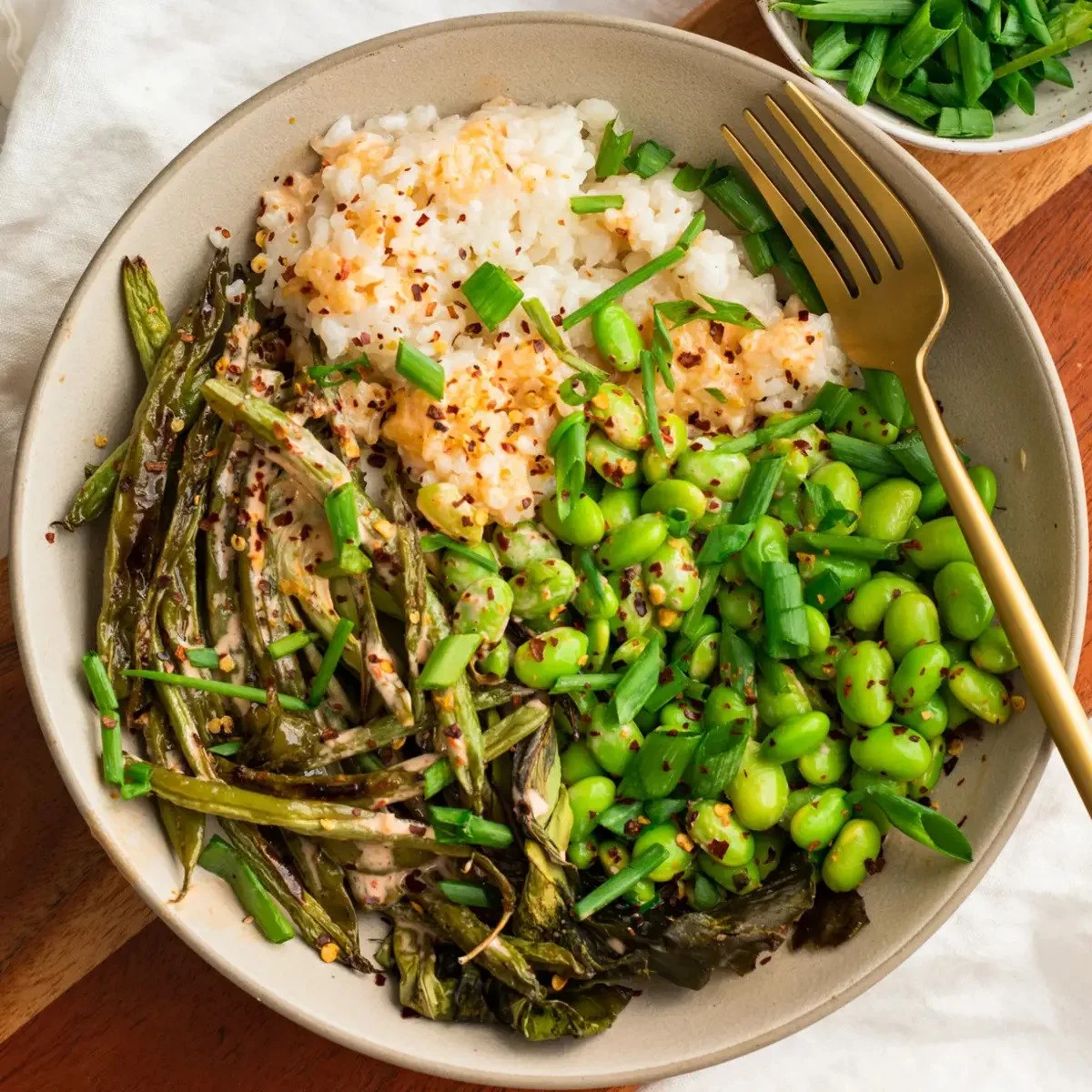A bowl of cooked green beans, mashed potatoes with gravy, and green peas garnished with chopped green onions, with a small bowl of chopped green onions on the side.