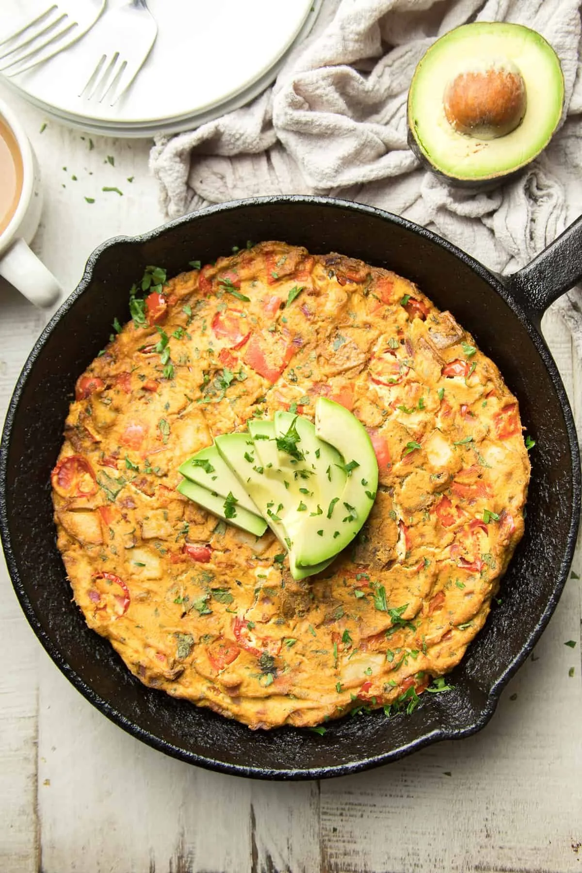 cast iron skillet with finished vegan frittata topped with avocado slices