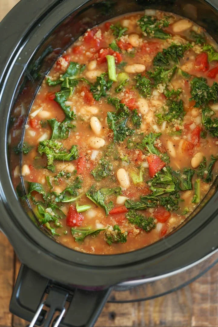 A bowl of vegetable soup with beans, kale, and tomatoes inside a slow cooker.