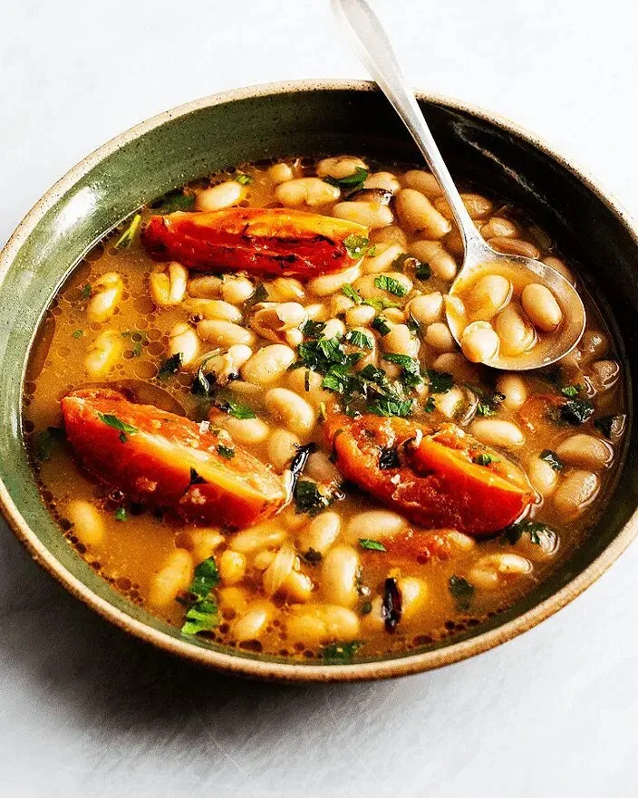 A bowl of bean and tomato soup garnished with chopped herbs, with a spoon inside.