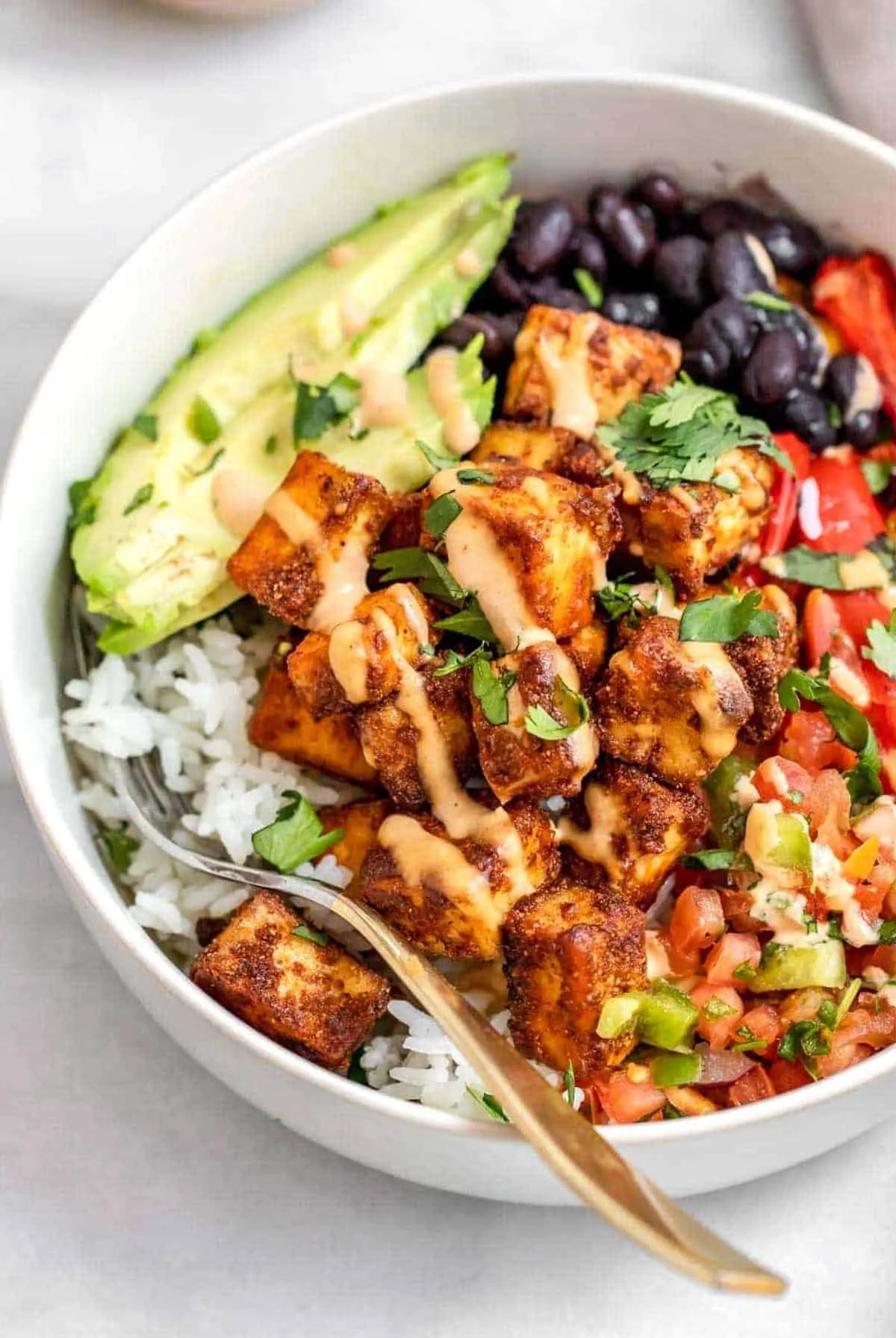 Bowl of food with tofu pieces, rice, avocado slices, black beans, tomato salsa, and chopped cilantro.