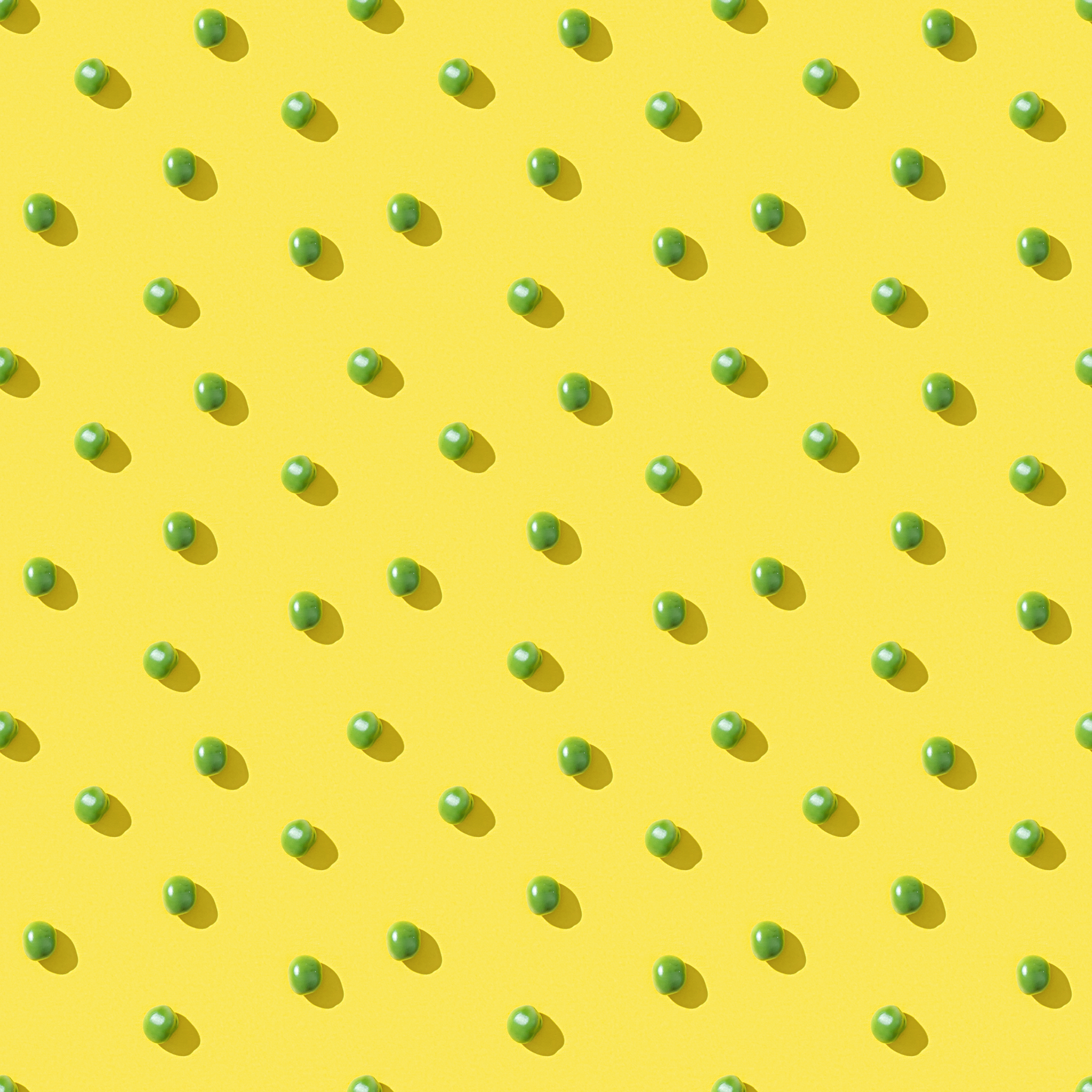 Peas arranged in a grid pattern on a yellow background, each casting a shadow.