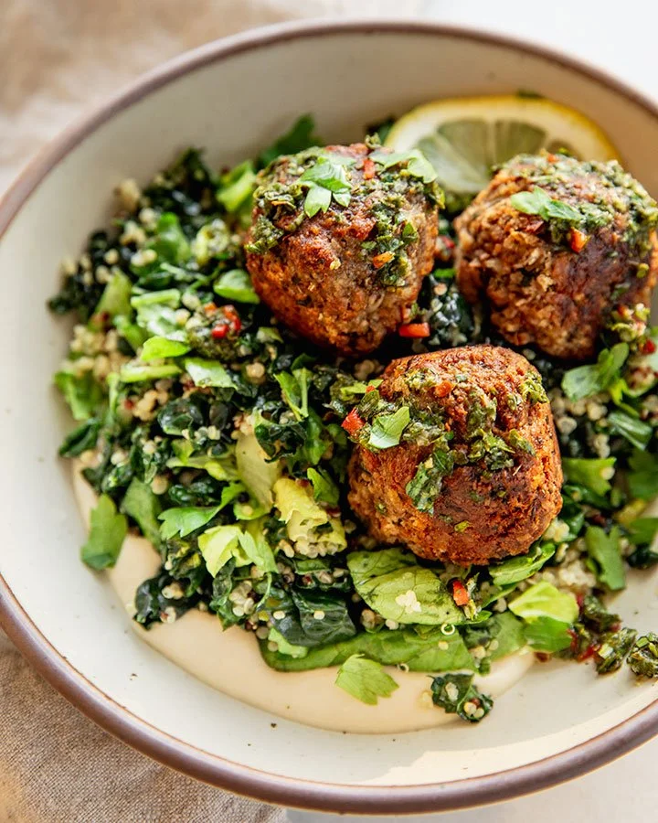 A bowl of Mediterranean food with three falafel balls topped with chopped herbs, served with a lemon wedge.