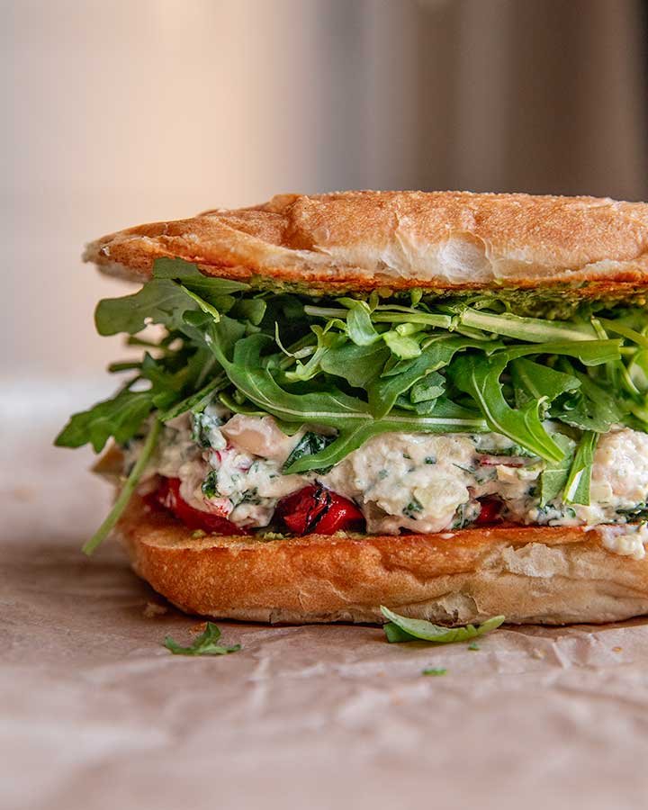 Close-up of a sandwich with fried bread, fresh arugula, and a creamy chicken and vegetable filling.