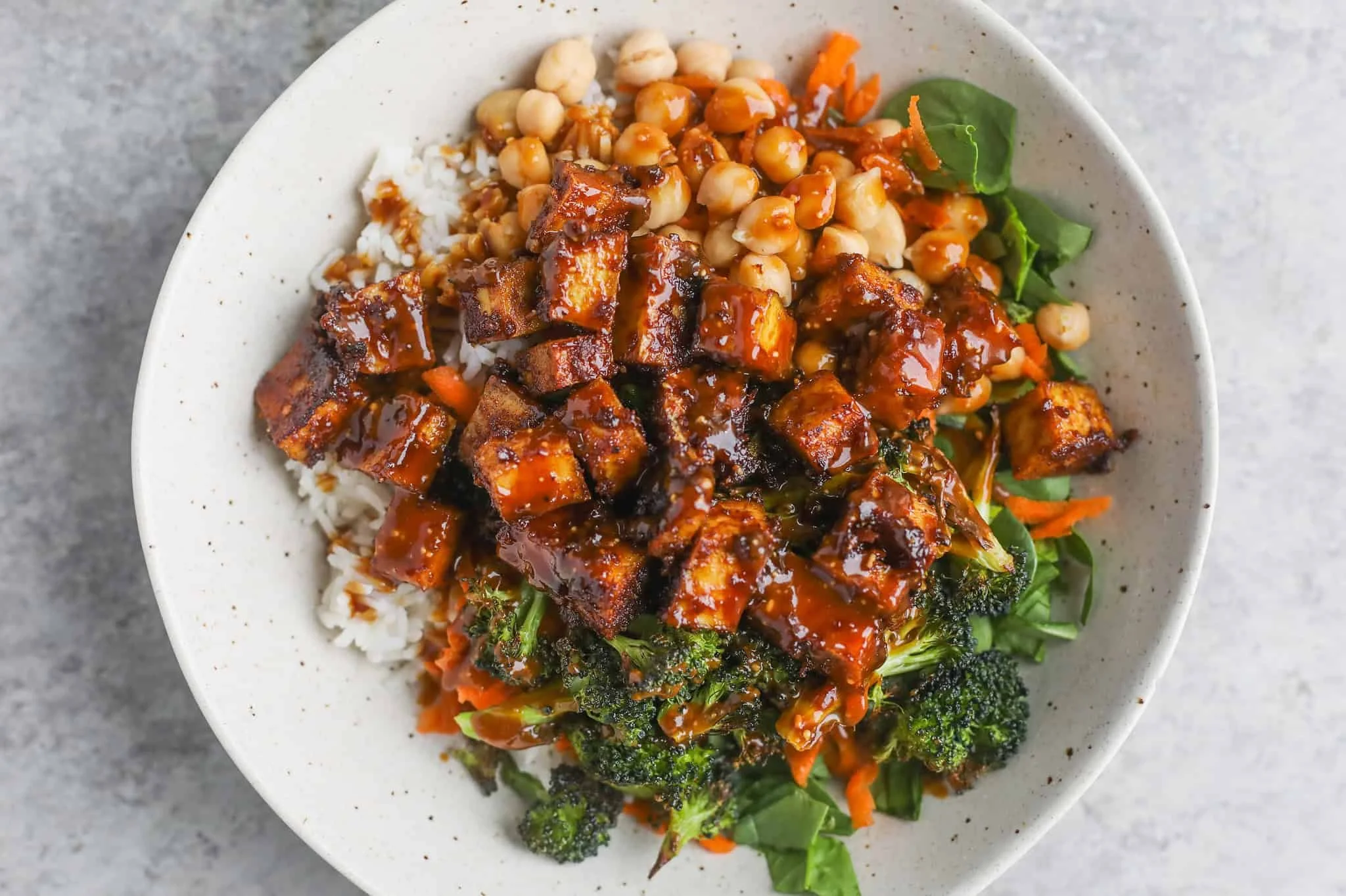 Bowl of rice topped with tofu, chickpeas, vegetables, and sauce