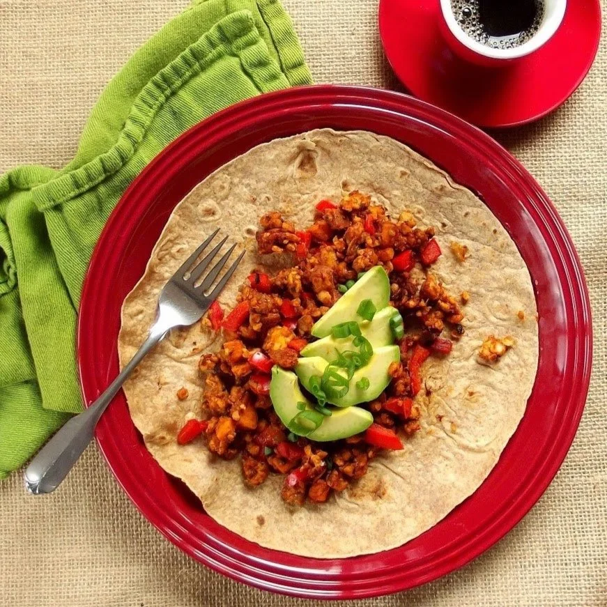 plate with sweet potato tempeh scramble on a flour tortilla topped with avocado and green onion
