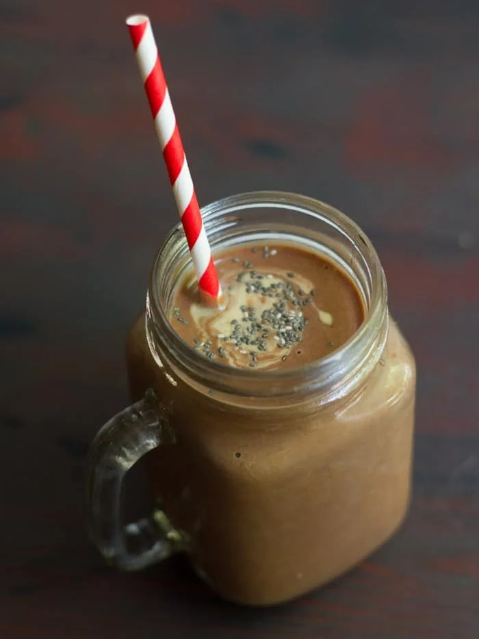 Mason jar mug filled with chocolate peanut butter chia smoothie and red and white striped straw