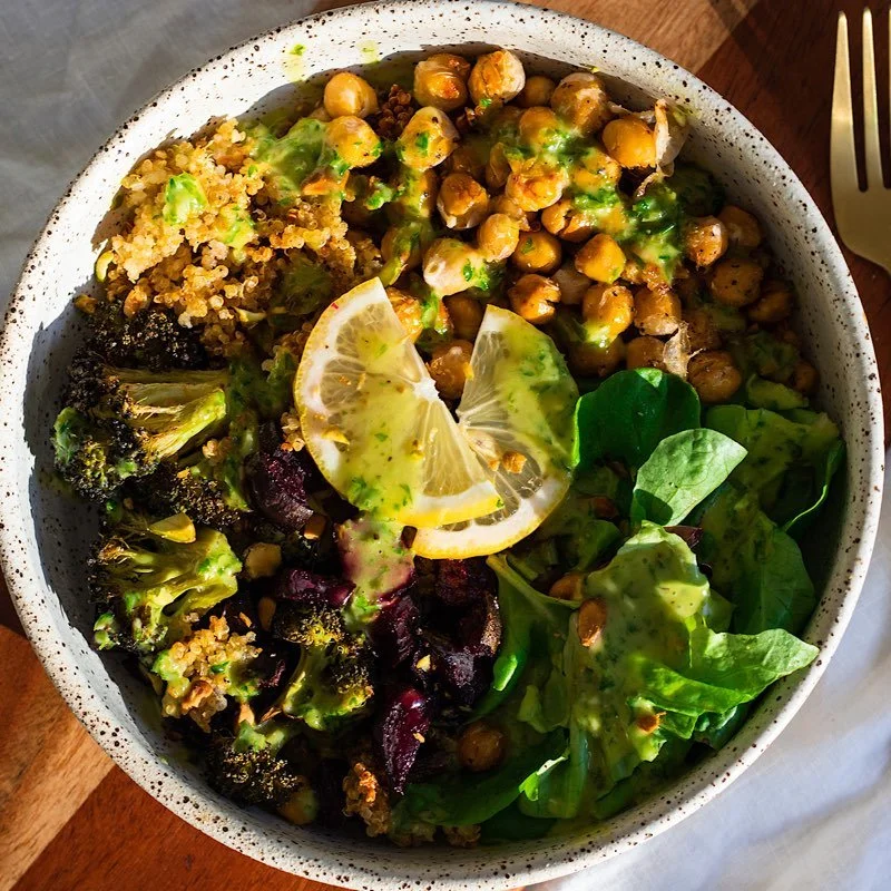 A bowl of salad with mixed greens, roasted chickpeas, roasted broccoli, quinoa, and lemon slices with green dressing.
