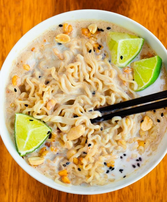 Bowl of ramen with noodles, corn, black sesame seeds, and lime wedges, with chopsticks resting on the noodles.