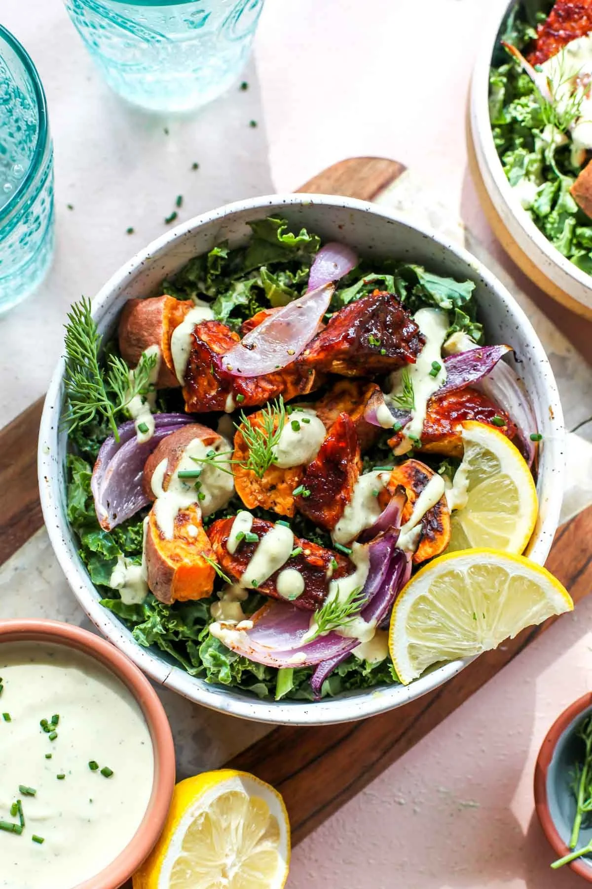 A bowl of grilled chicken salad with lemon slices, served with a side of creamy dressing and glasses of water.