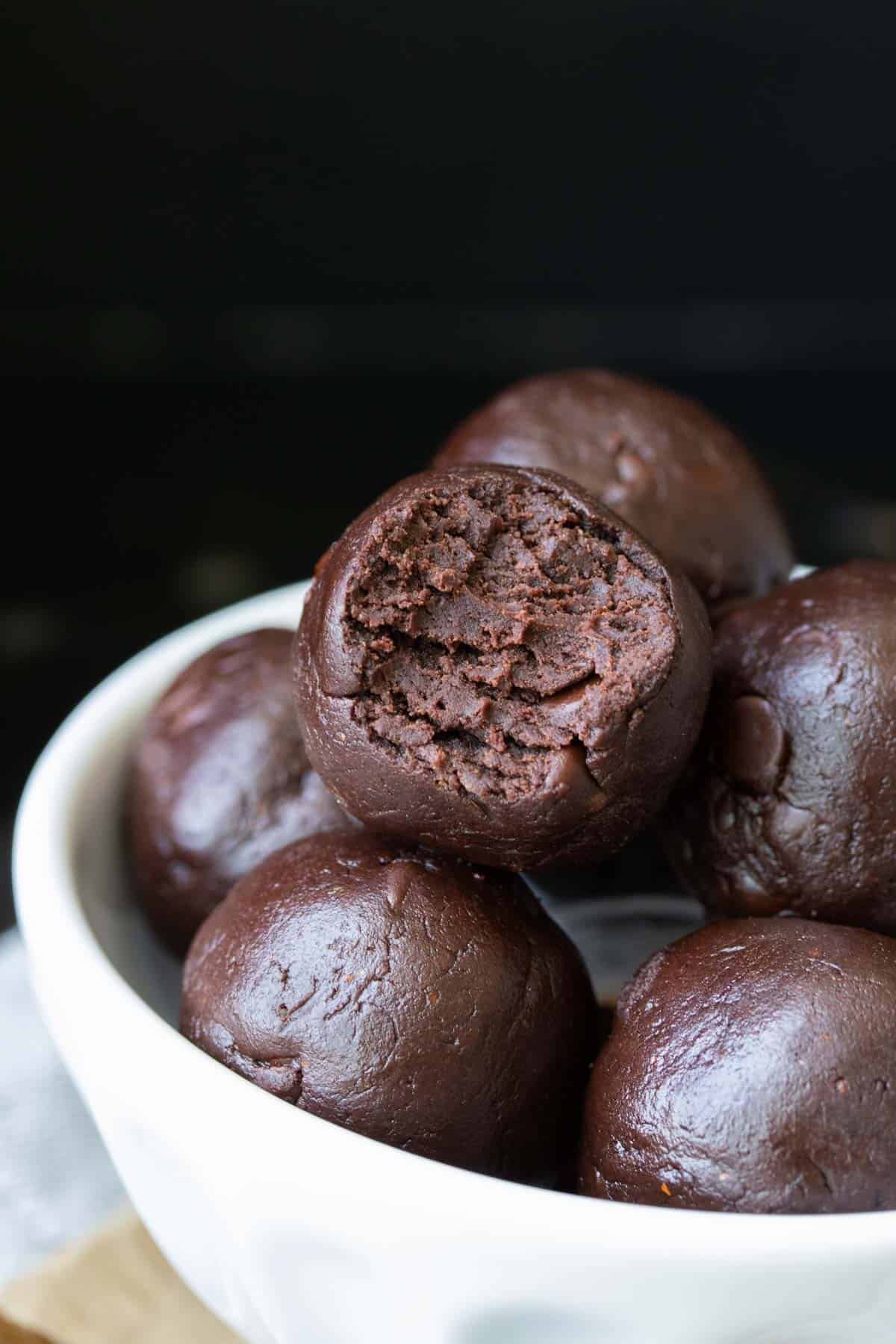 Close-up of chocolate truffles in a white bowl, one of which is broken open showing the soft interior.