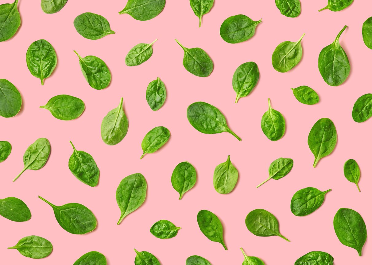 Pattern of various fresh green spinach leaves scattered on a pink background.