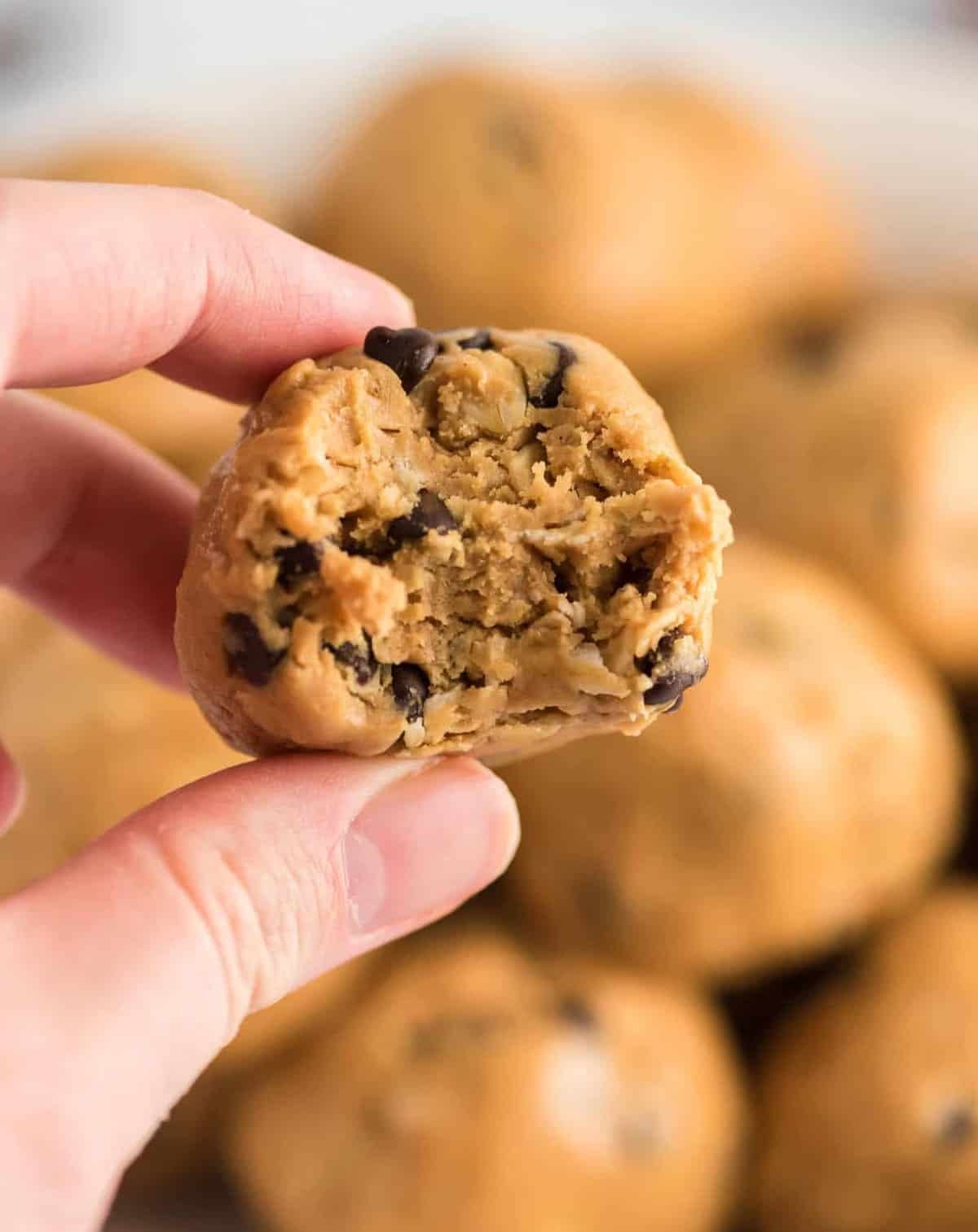 Close-up of a hand holding a vegan chocolate chip cookie with a background of more cookies.