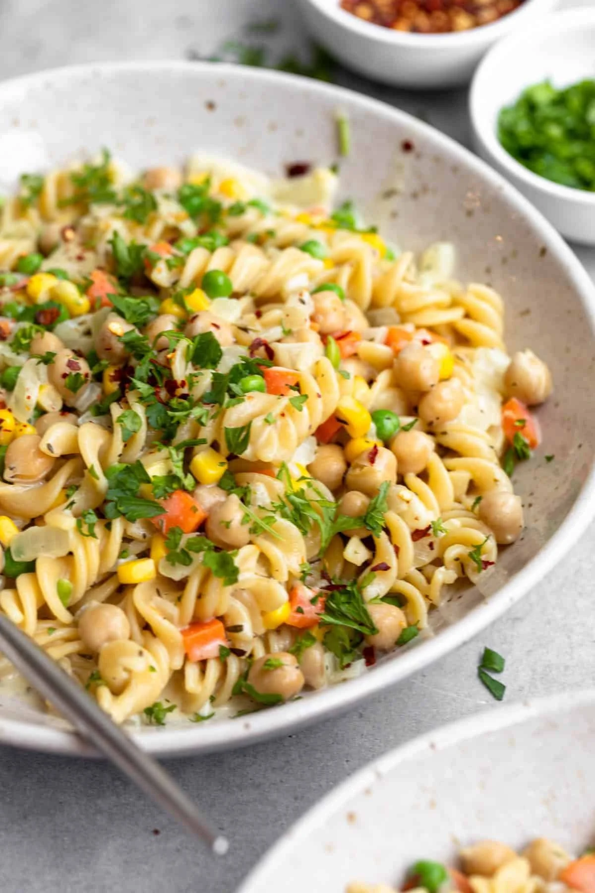A bowl of vegetable pasta salad with chickpeas, carrots, corn, and chopped herbs