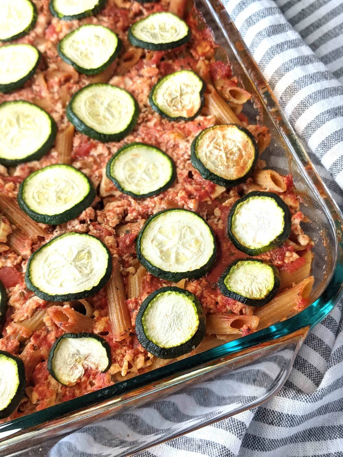 Unbaked zucchini and pasta casserole in a glass dish, topped with sliced zucchini.