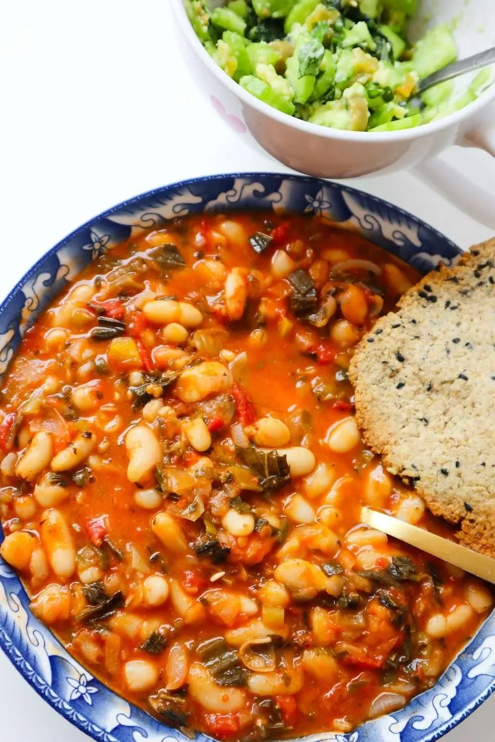 Close-up of a bowl of bean soup with vegetables, a side of cornbread, and a bowl of chopped lettuce salad.