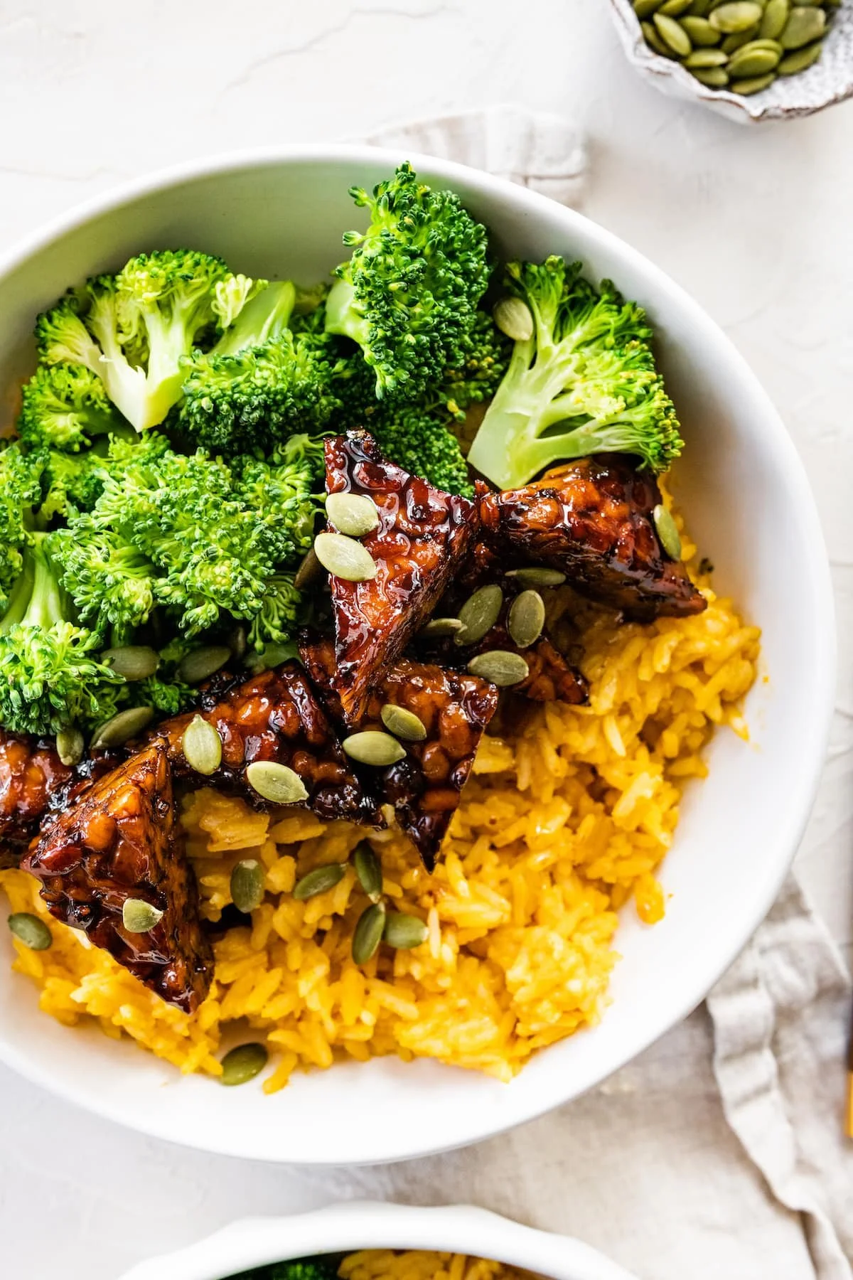 Bowl of broccoli, yellow rice, teriyaki tofu with pumpkin seeds.