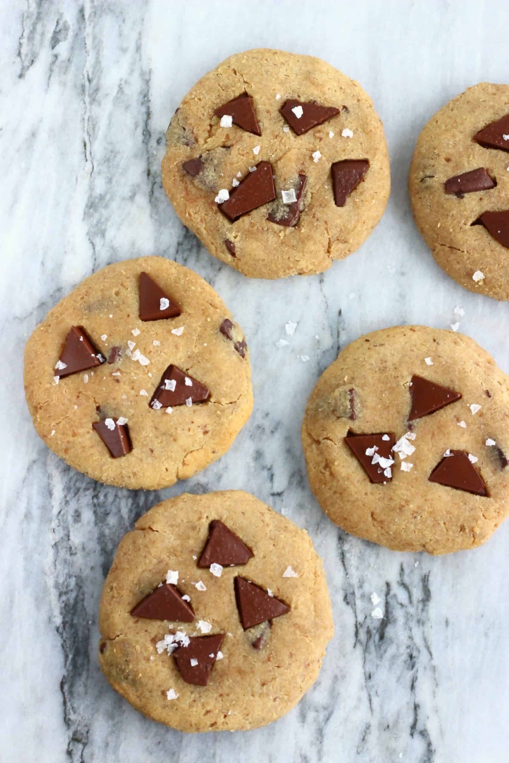 Four vegan chocolate chip cookies with sea salt on a marble surface.