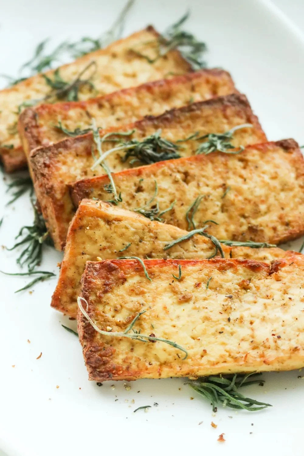 Slices of mediterranean seasoned tofu on a white plate, garnished with herbs.