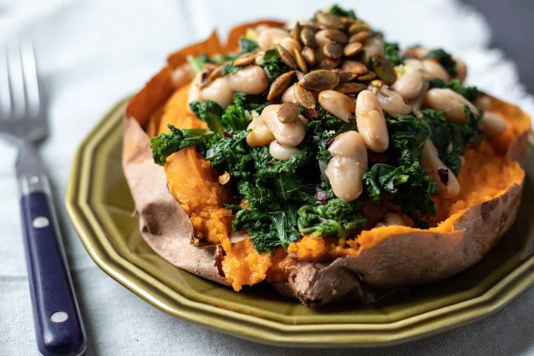 Sweet potato loaded with sautéed greens and sunflower seeds on a green plate.
