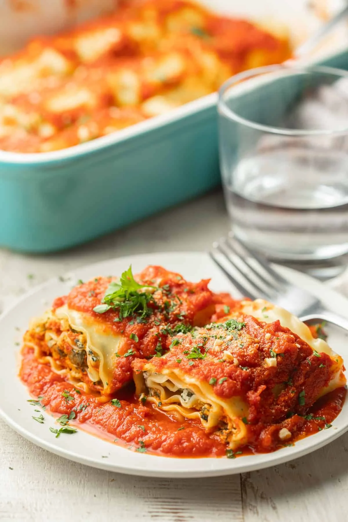 two plated vegan spinach lasagna roll ups topped and in a bed of red sauce