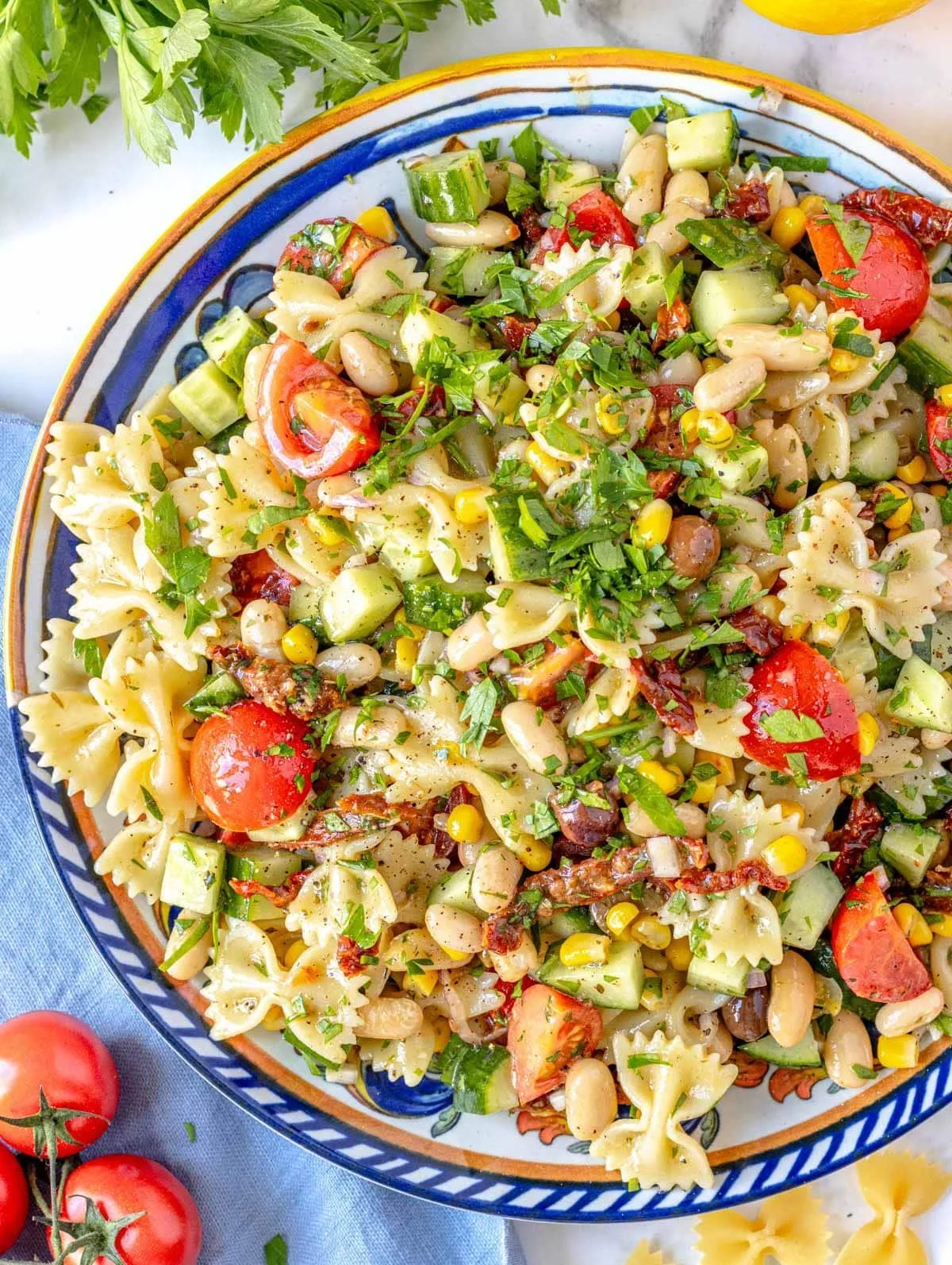 A colorful pasta salad with cherry tomatoes, cucumbers, kidney beans, corn, and fresh herbs.