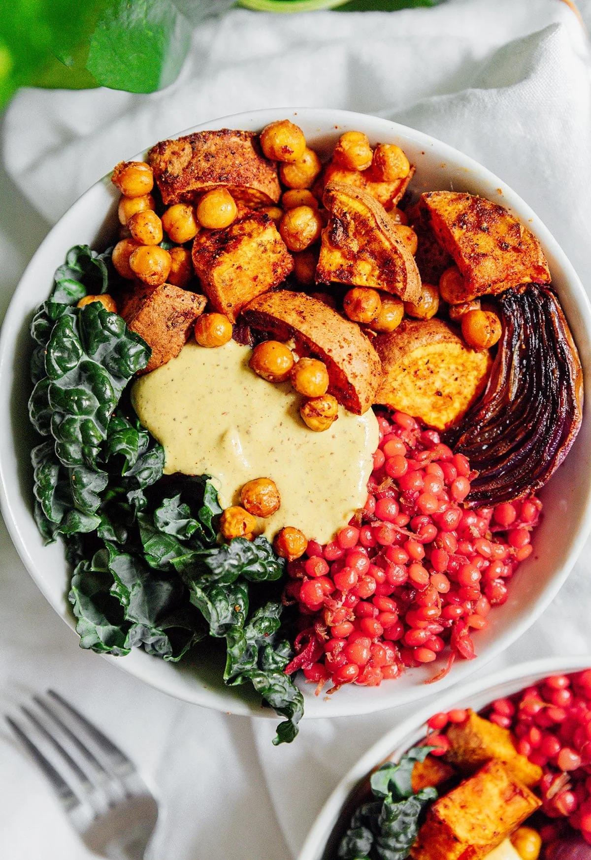 A bowl of roasted sweet potatoes, chickpeas, red onion, collard greens with creamy yogurt sauce, and red lentils.