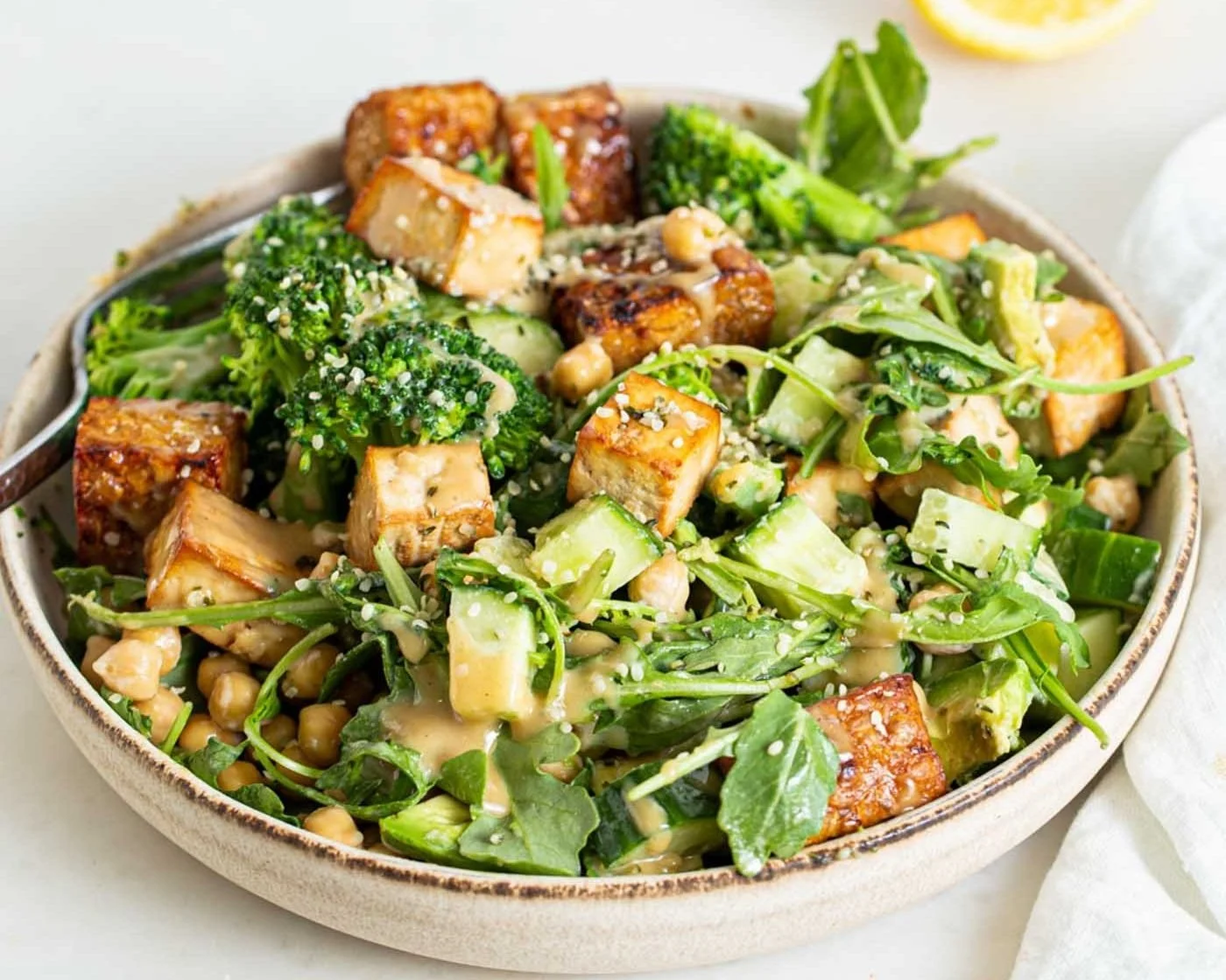 Salad bowl with broccoli, grilled tofu, greens, chickpeas, cucumber, and a creamy dressing.