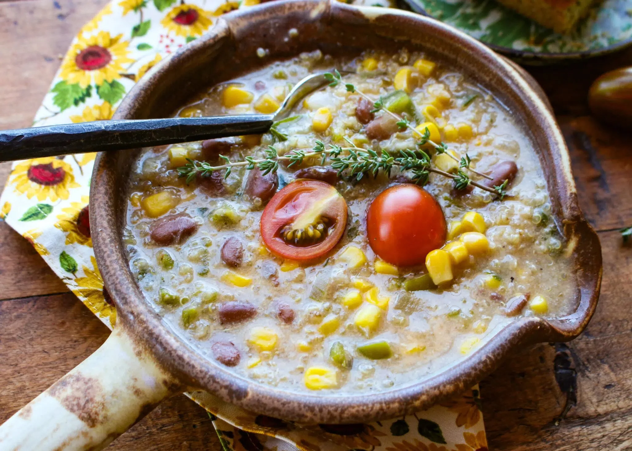 A bowl of creamy vegetable and bean soup garnished with a cherry tomato, a slice of tomato, corn, herbs, and a sprig of thyme.