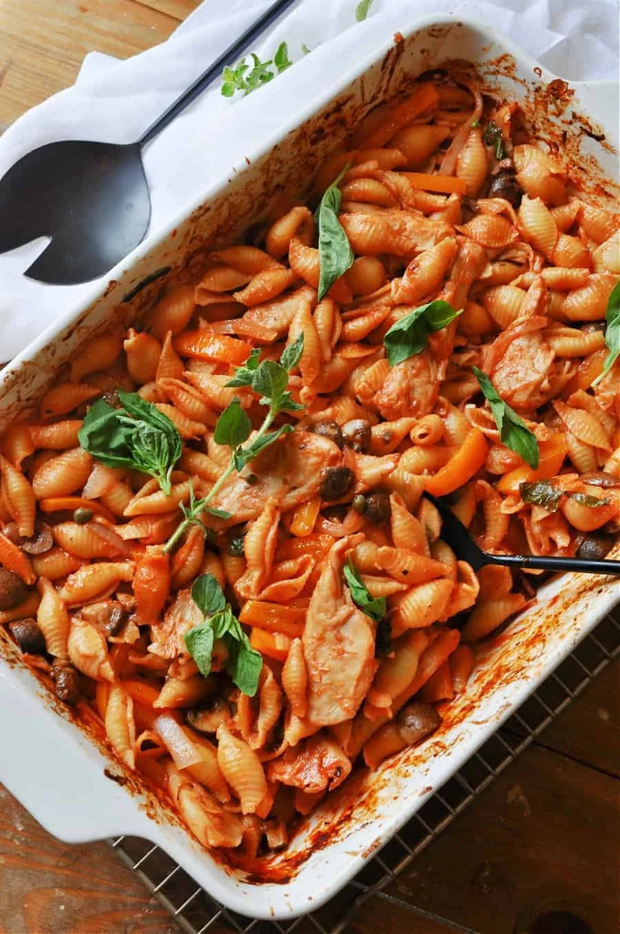 Baked pasta with tomato sauce, garnished with basil leaves in a white casserole dish.