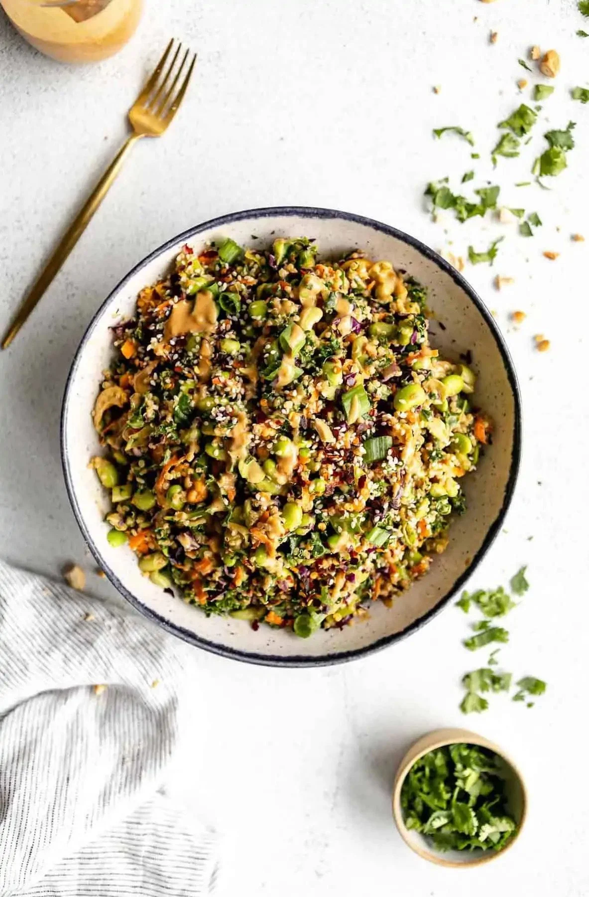 Bowl of chopped salad with greens, vegetables, and a nut or seed topping, served with a fork and scattered herbs.