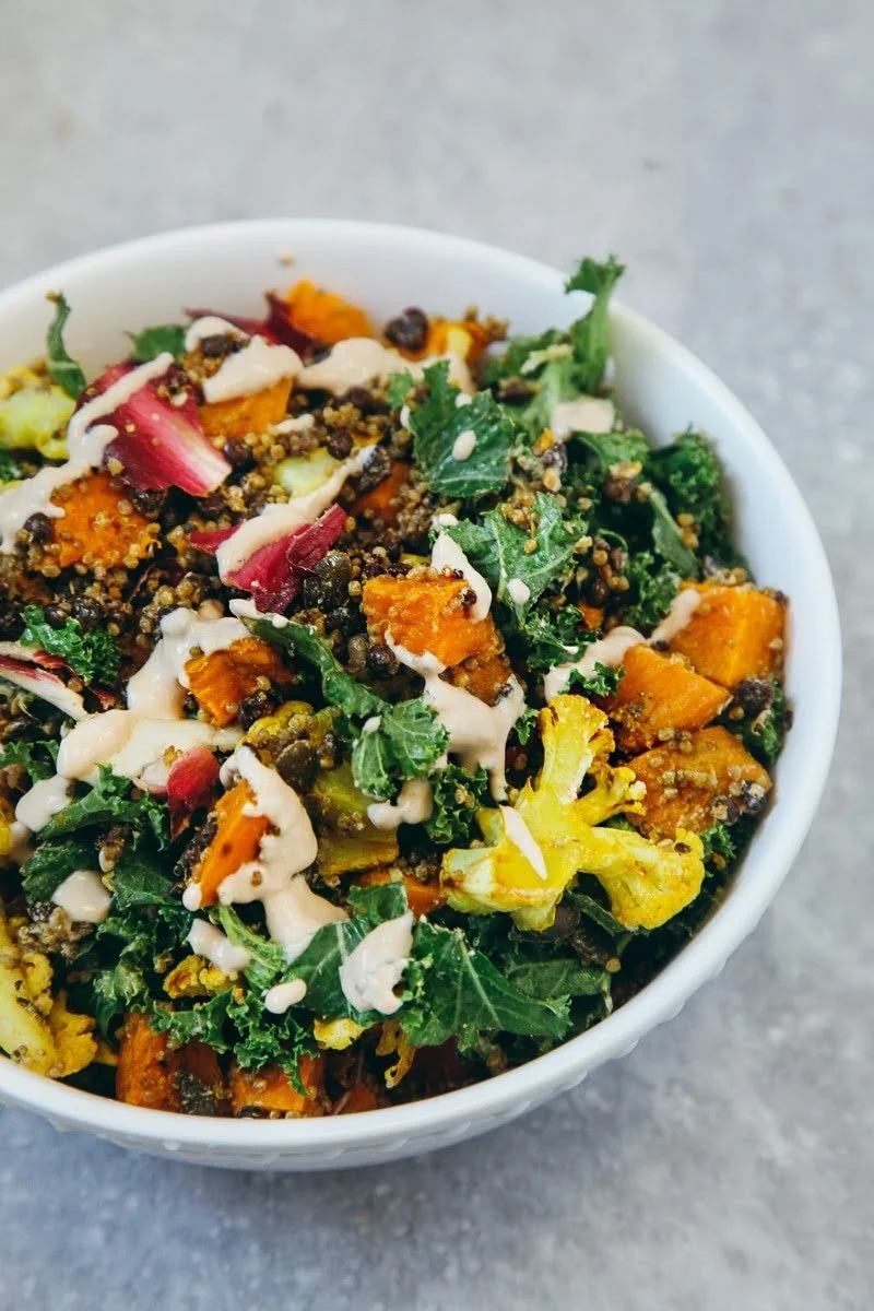 Close-up of a bowl of kale salad with roasted sweet potatoes, radishes, and drizzled with dressing.