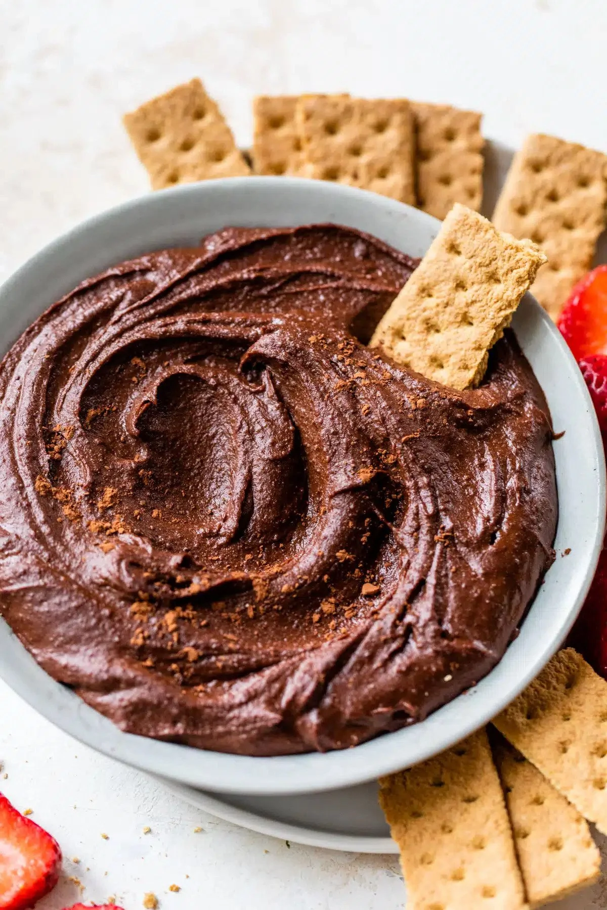 Vegan Chocolate hummus in a white bowl garnished with graham cracker sticks, strawberries, and more graham crackers in the background.