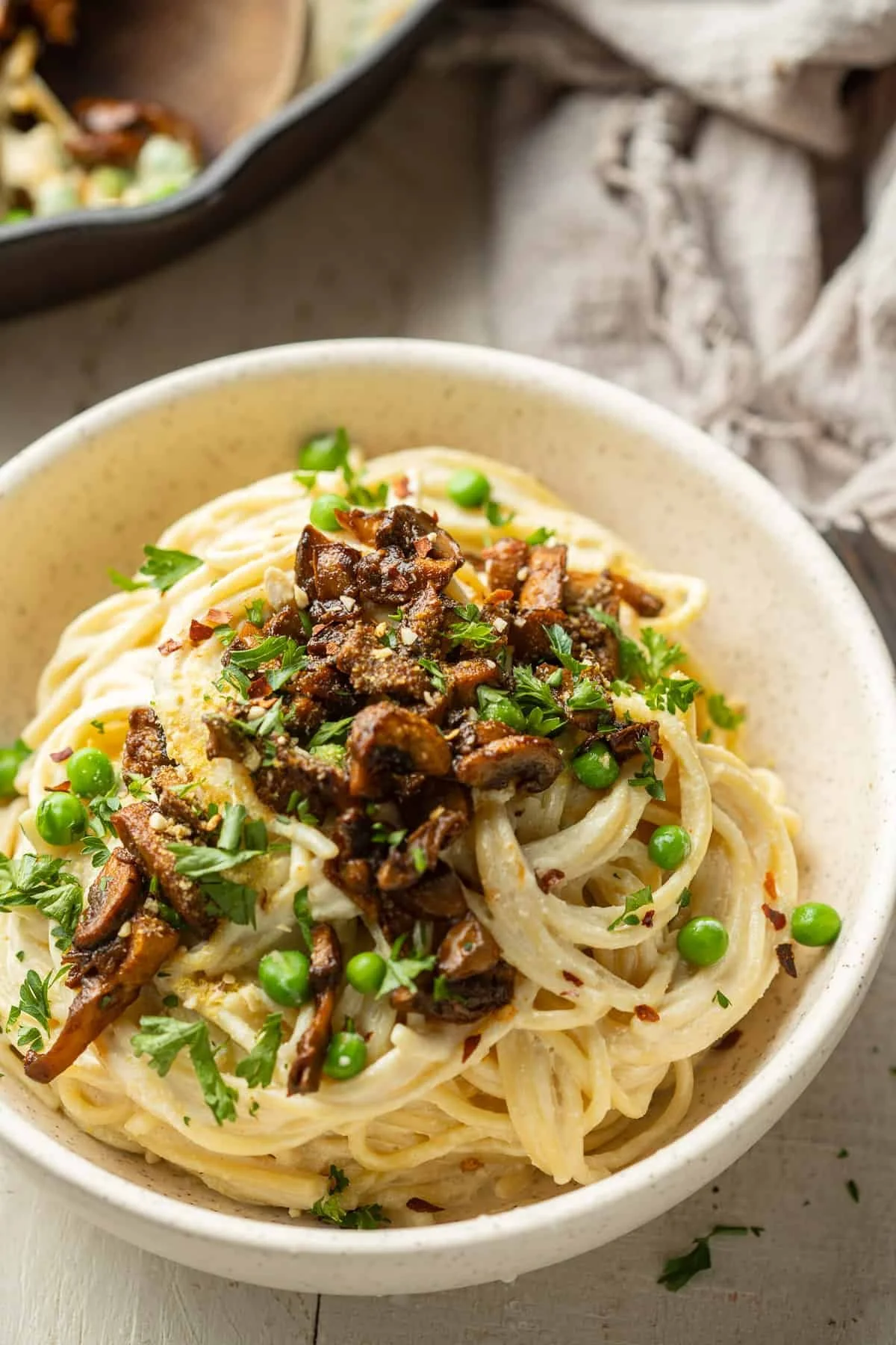 plate of vegan spaghetti carbonara topped with peas and mushrooms