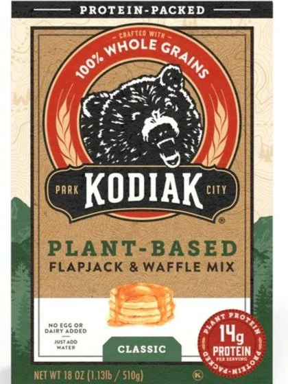 Packaging of Kodiak plant-based flapjack and waffle mix with a bear logo and labeling for protein, whole grains, and no added eggs or dairy.