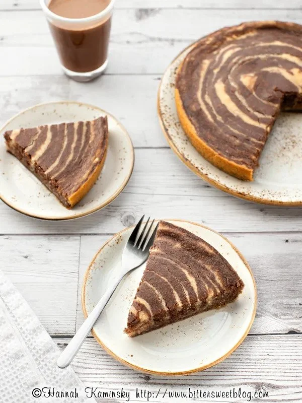 A marble cake with chocolate and vanilla layers, served on white plates with a fork, accompanied by a glass of chocolate milk on a white wooden table.