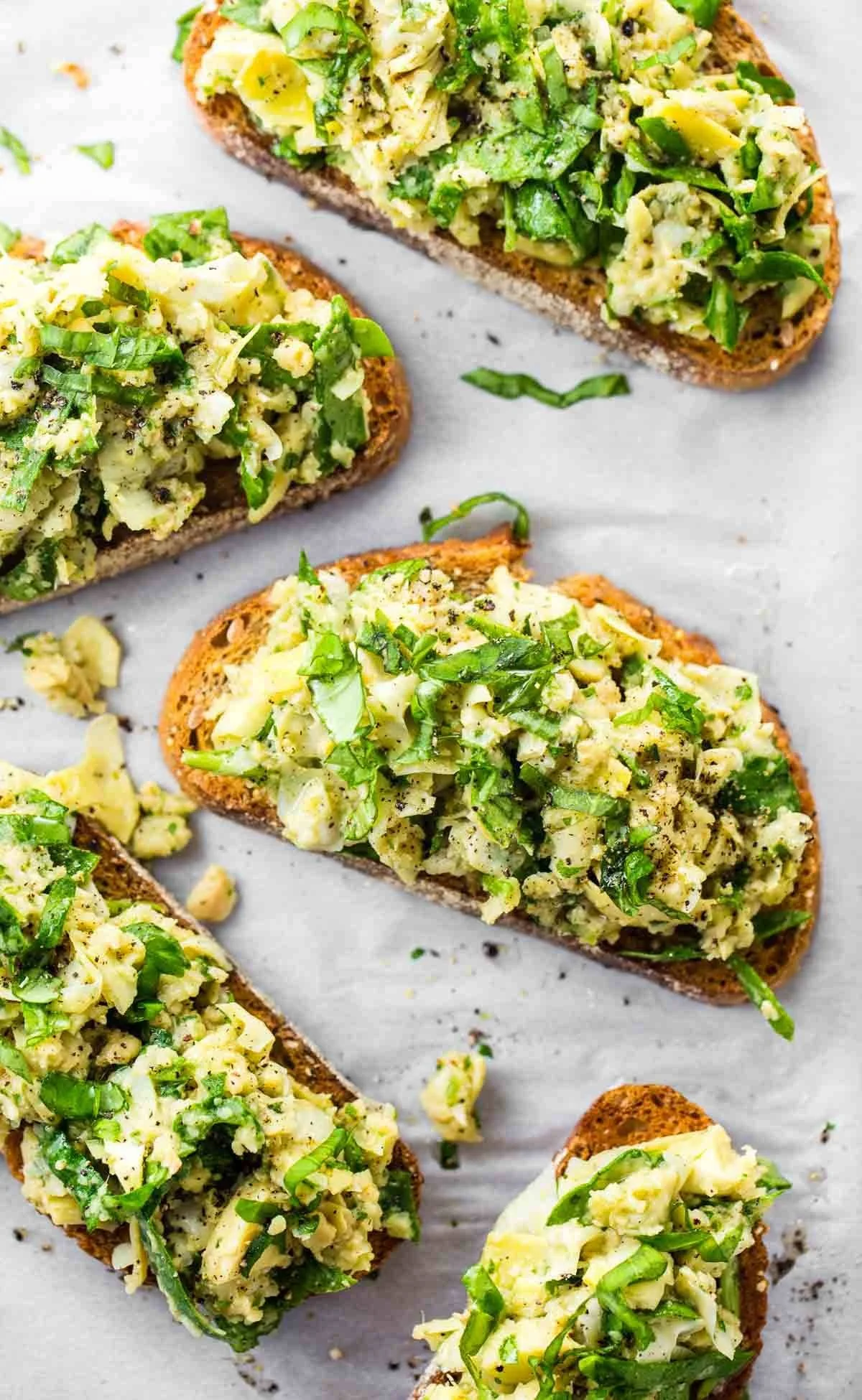 Close-up of avocado egg salad served on toast, garnished with chopped green herbs and black pepper.