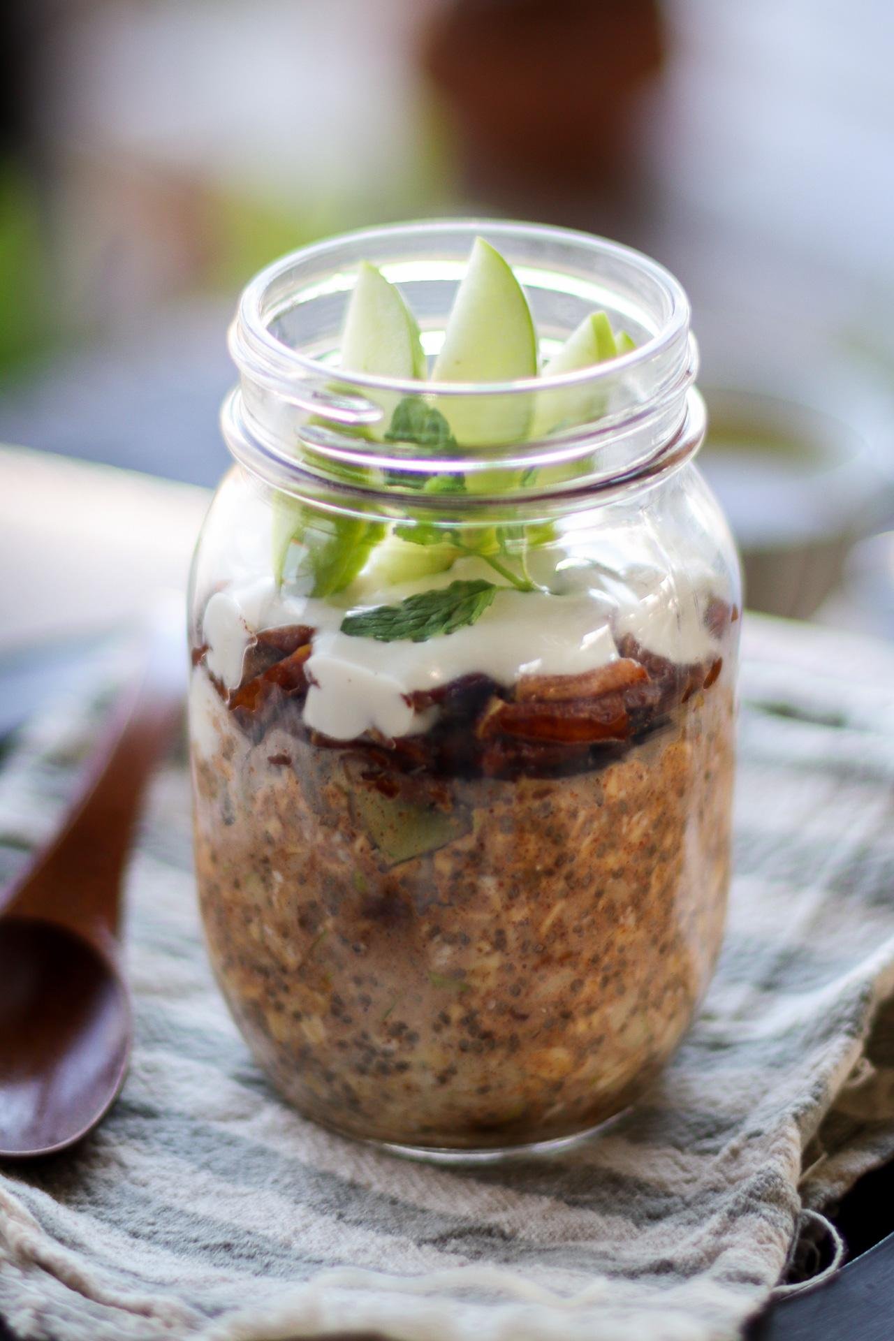 A jar layered with granola, yogurt, and fresh apple slices on top.