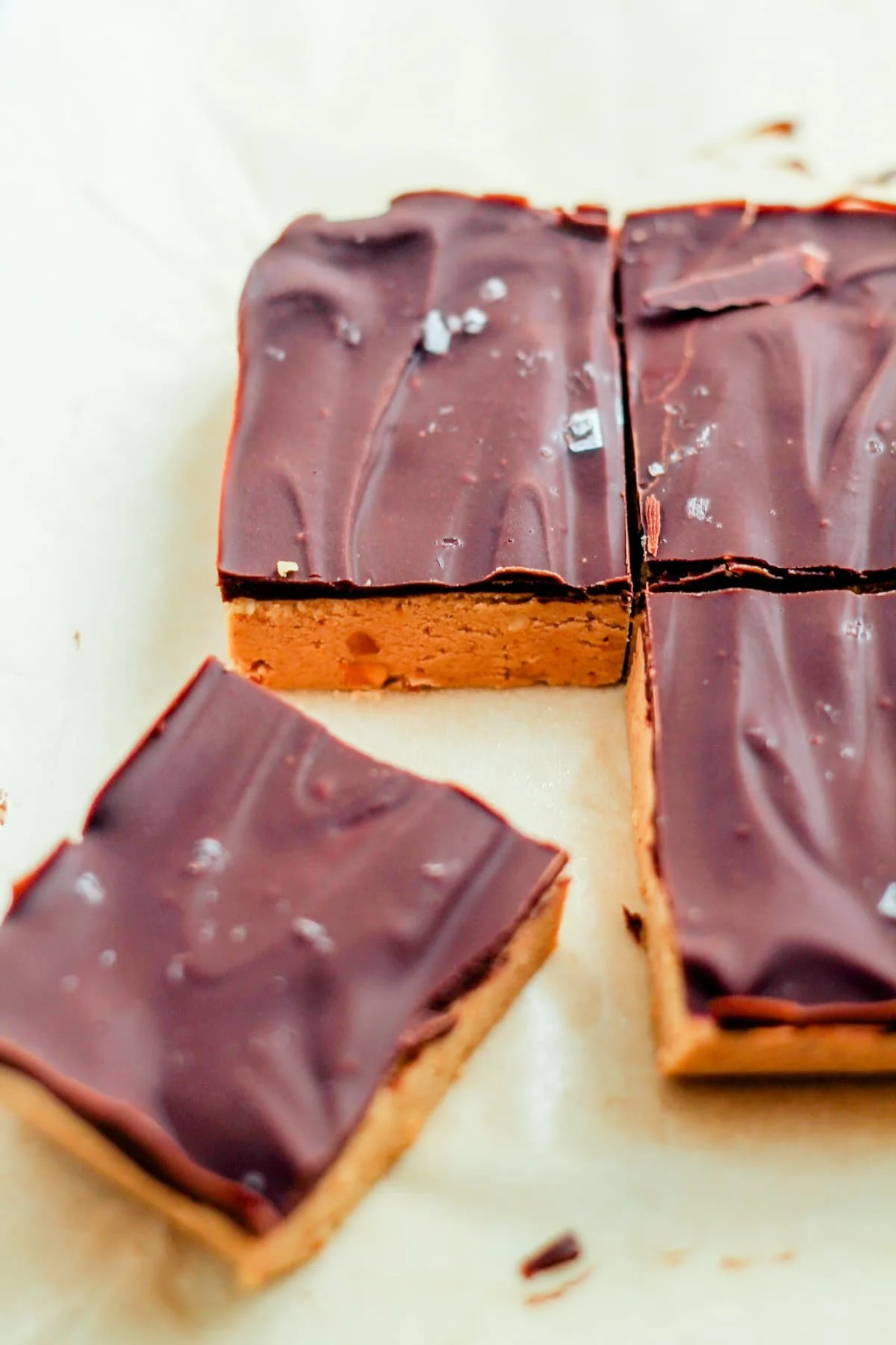 Three chocolate-covered caramel squares on a white surface, one piece slightly separated revealing the caramel inside.
