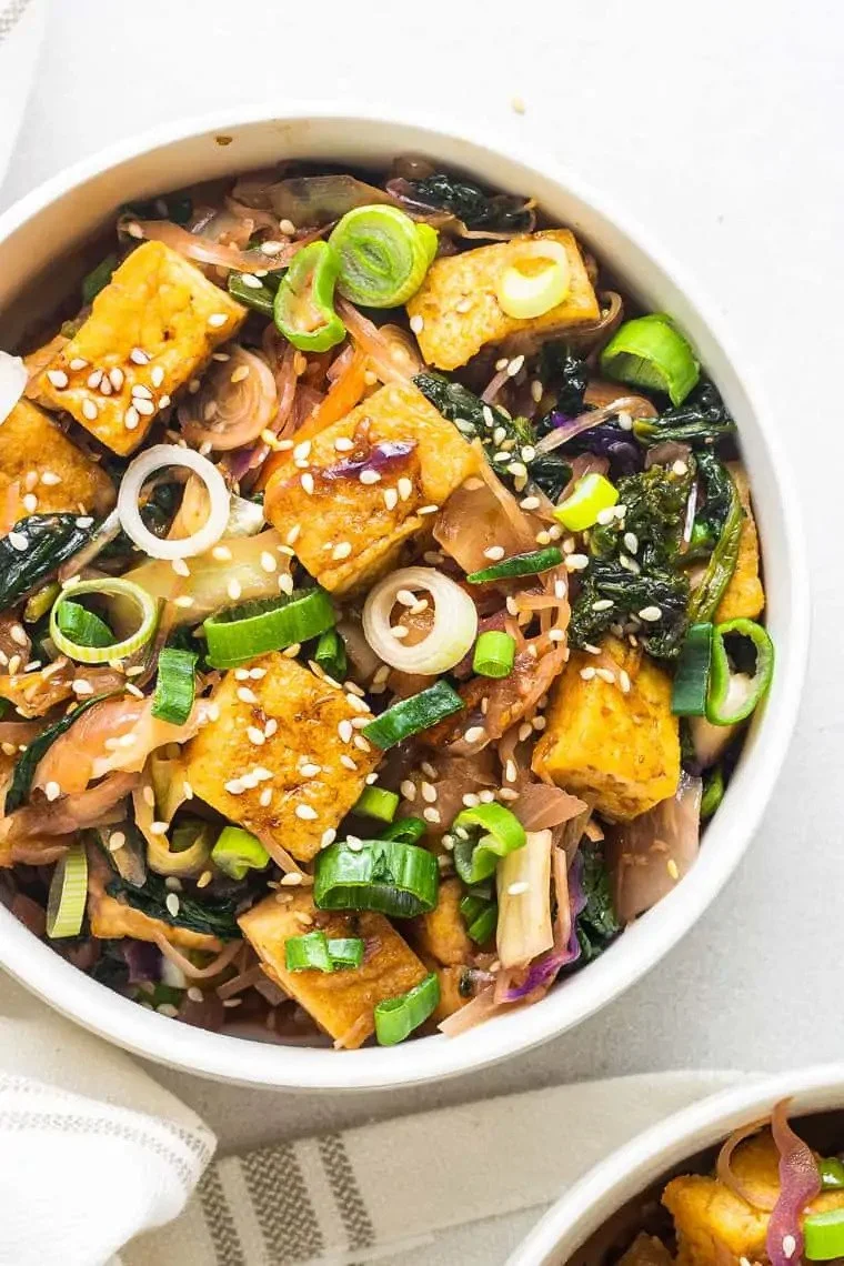 Bowl of tofu salad with green onions, sesame seeds, and mixed vegetables.