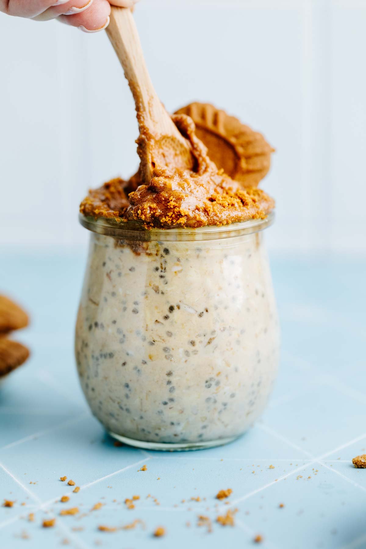 A glass jar filled with vegan cookie dough, topped with a scoop of cookie dough and crushed cookies.