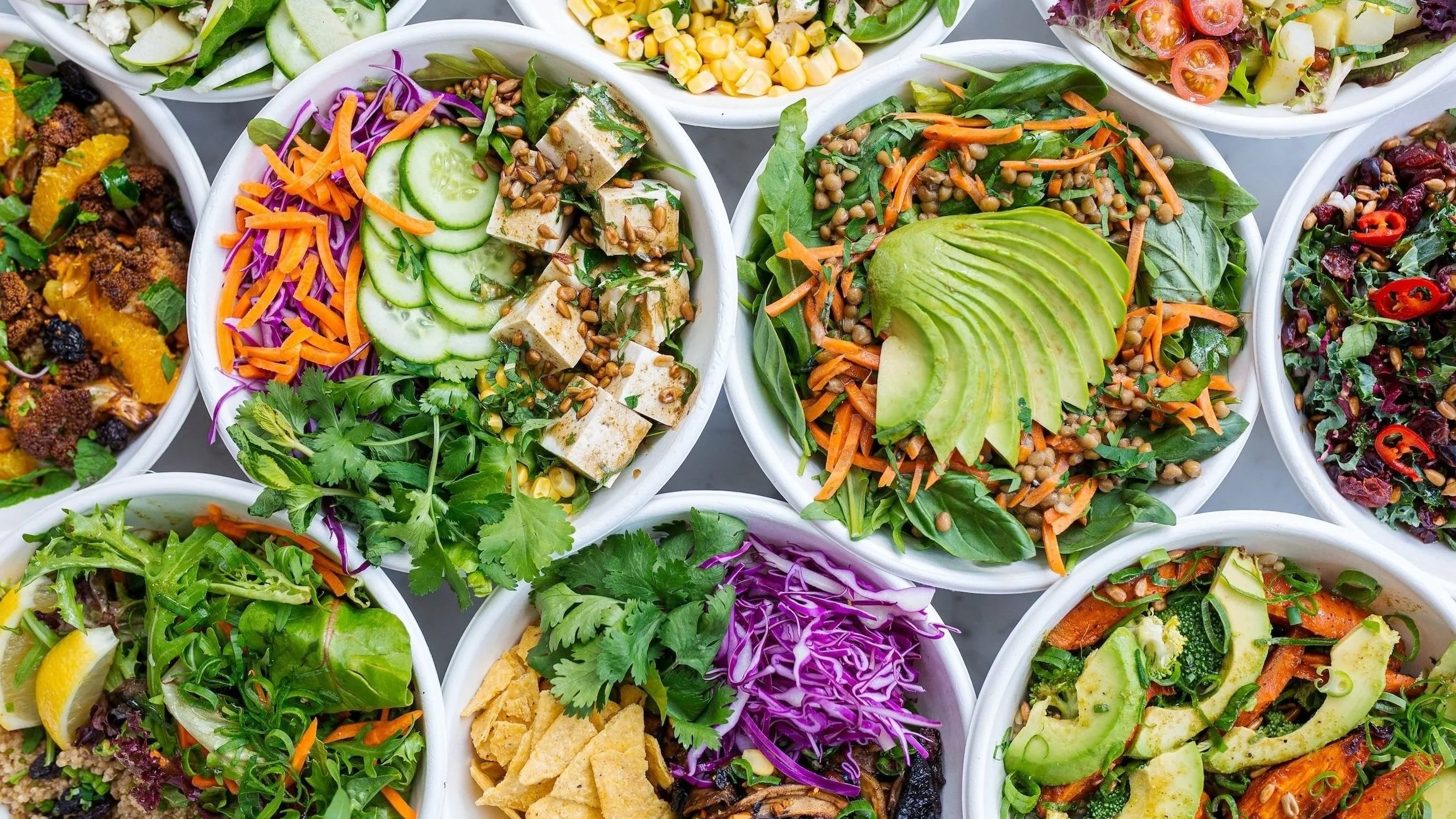 Several bowls of colorful salads with various fresh vegetables, greens, and toppings.