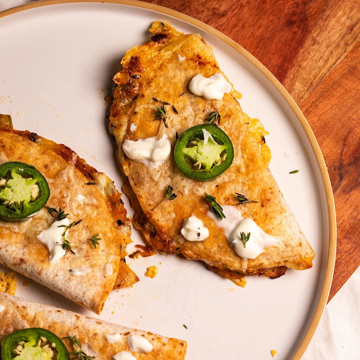 Two slices of grilled quesadillas topped with sour cream, sliced jalapeños, and fresh herbs on a white plate.