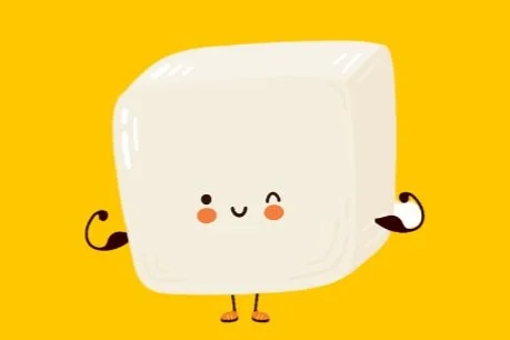 Cute cartoon tofu character flexing muscles with a smiling face, small arms, and legs, against a yellow background.