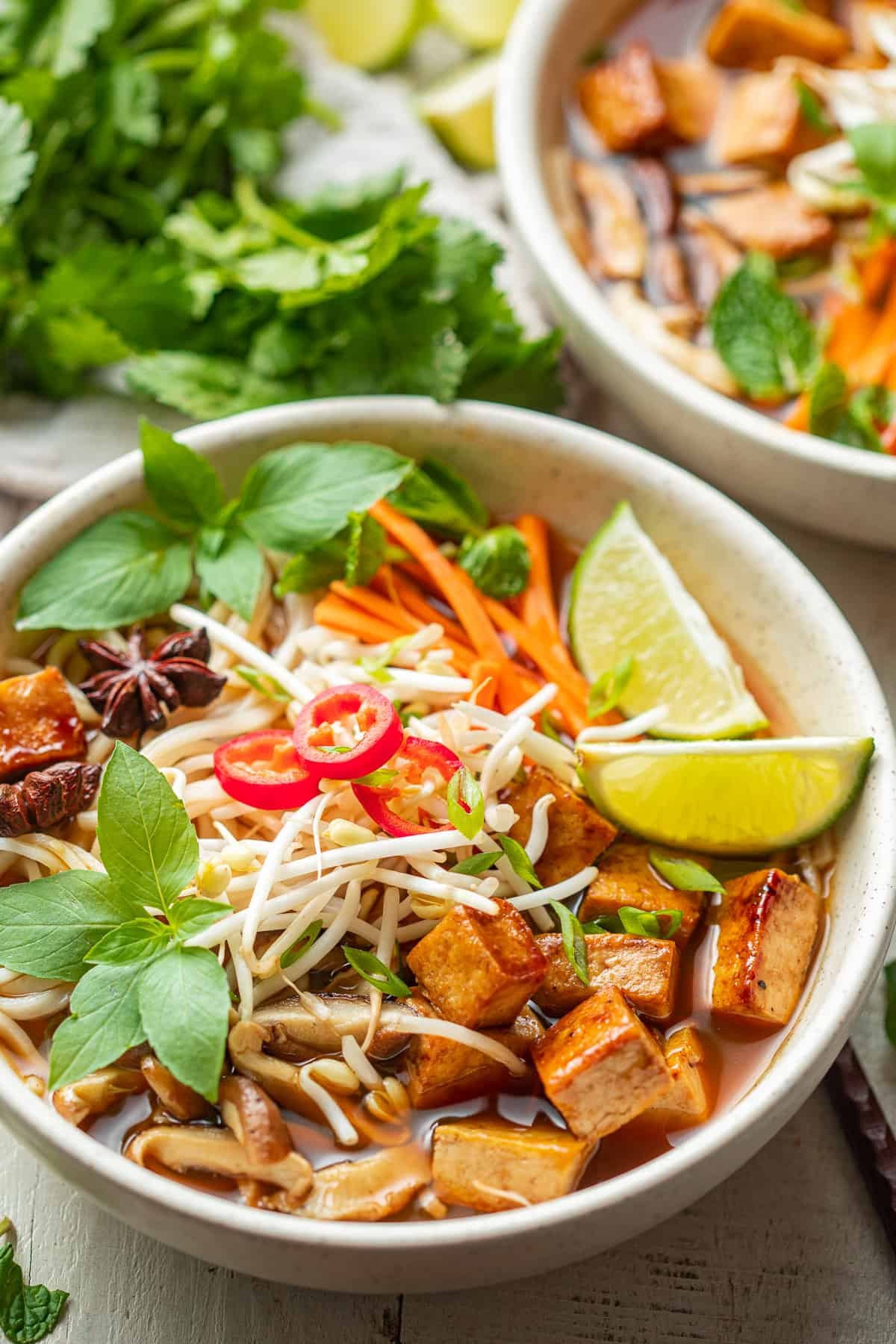 bowl of vegan pho with tofu and beansprouts side of lime wedges